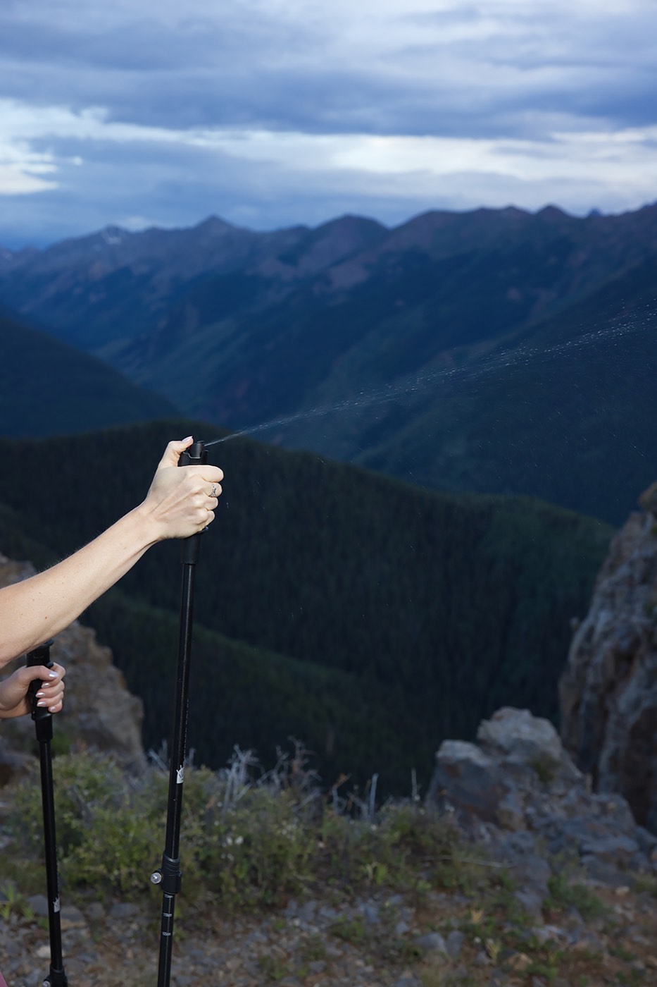 A hiker discharging the spray from a Pepper Poles handle over a mountain valley